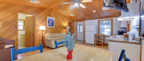 A spacious room with a wooden ceiling, a dining table, chairs, a sofa, and a kitchen area.