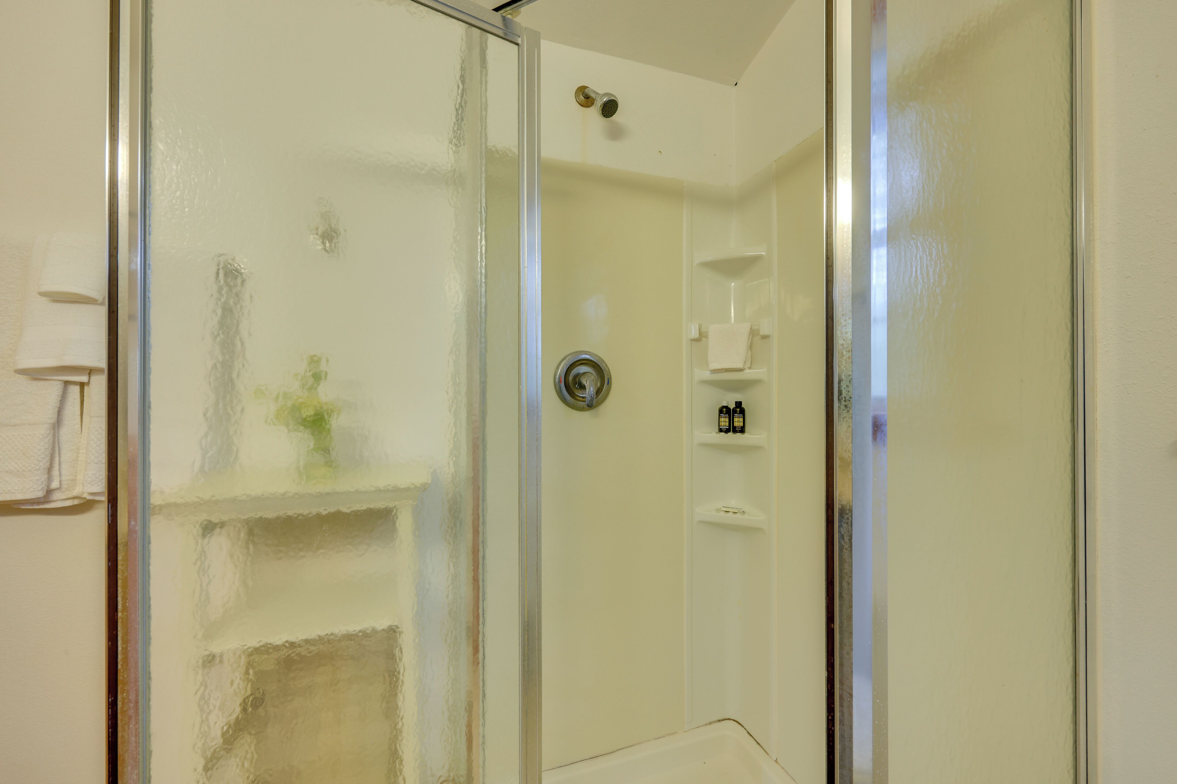 Un baño con cabina de ducha de vidrio, un lavabo blanco y un estante con artículos de aseo.