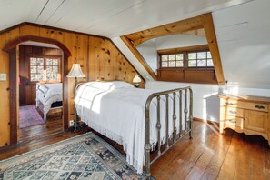Ein Schlafzimmer mit Holzboden, einem Bett mit weißer Bettdecke, einem Nachttisch, einer Kommode und einem Fenster.