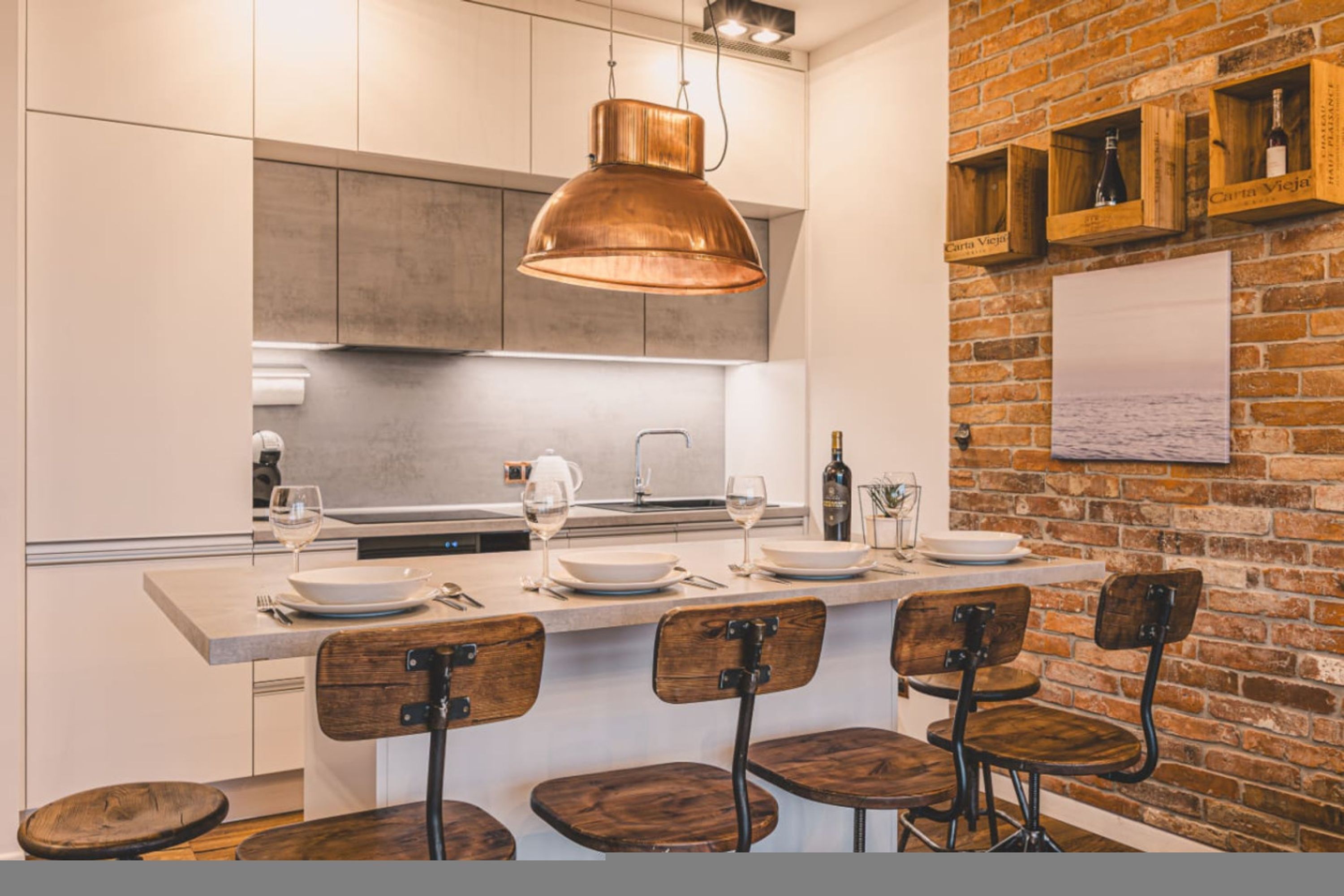Une cuisine moderne dotée d’un grand îlot central, de tabourets de bar et d’un luminaire suspendu en cuivre.