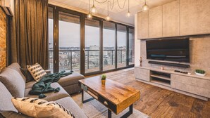 Un salon moderne doté d’un grand téléviseur, d’un canapé, d’une table basse et offrant une vue sur la ville grâce à de grandes fenêtres.