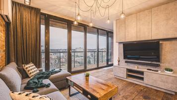 A modern living room with a large TV, a sofa, a coffee table, and a view of the city through large windows.