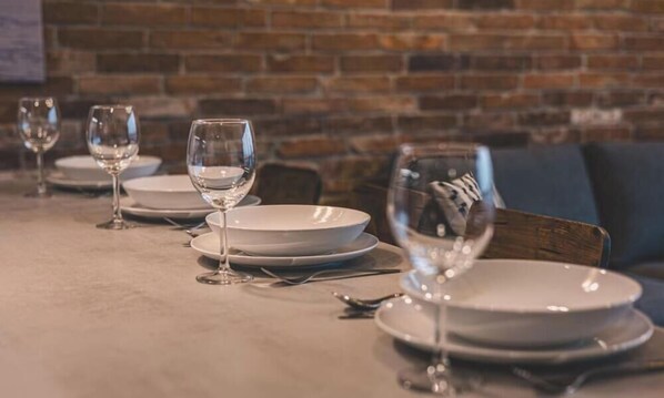 A dining table set with plates, glasses, and cutlery, with a brick wall in the background. - Ladrillo - Luksusowy Loft z Widokiem na Miasto (Bydgoszcz)