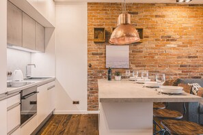 A modern kitchen with a brick wall, stainless steel appliances, and a wooden dining area. - Ladrillo - Luksusowy Loft z Widokiem na Miasto (Bydgoszcz)