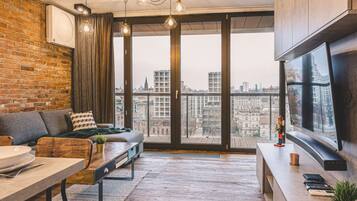 A modern living room with a sofa, a dining table, and a large window offering a city view.
