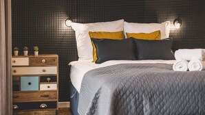 A neatly made bed with a quilted cover, a wooden nightstand with drawers, and a wall with a textured pattern. - Ladrillo - Luksusowy Loft z Widokiem na Miasto (Bydgoszcz)
