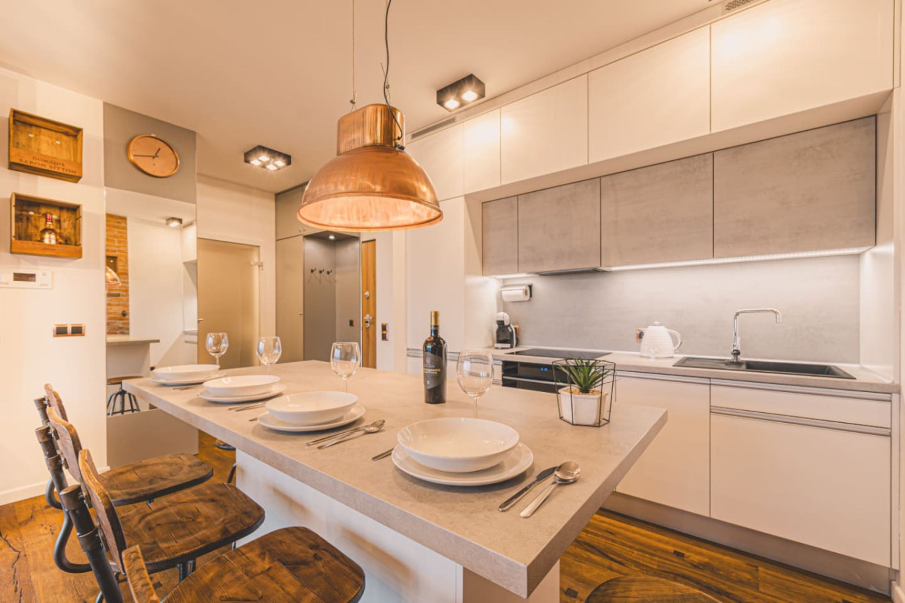 Una cocina moderna con una isla central, sillas de madera, una lámpara colgante de cobre y un horno empotrado.