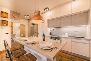 A modern kitchen with a central island, wooden chairs, a hanging copper pendant light, and a built-in oven. - Ladrillo - Luksusowy Loft z Widokiem na Miasto (Bydgoszcz)