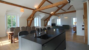 A spacious kitchen with a large island, wooden beams, and a view of the living area.