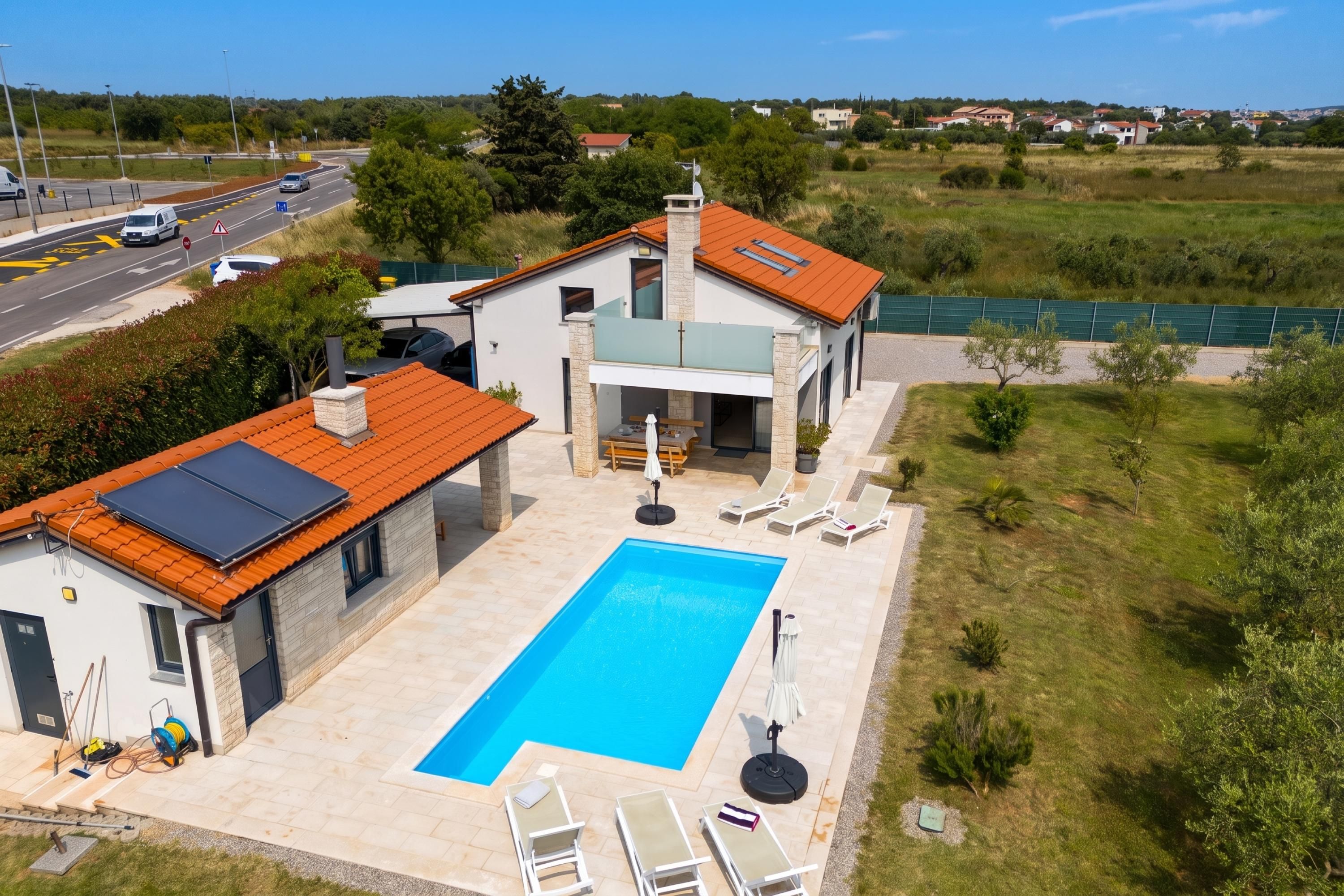 Et moderne hus med en swimmingpool, en overdækket terrasse og udsigt til en vej med biler.