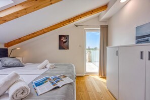 A bedroom with a sloped ceiling, a bed with white linens, a magazine on the bed, and a view through a glass door to the outside. - Sea View Villa Maria With Pool (Medulin)