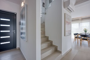 A modern interior with a staircase, a dining area with a table and chairs, and a door with illuminated panels. - Sea View Villa Maria With Pool (Medulin)