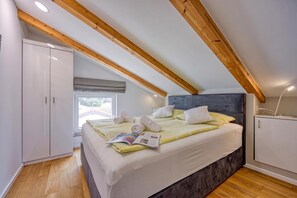 Ein Schlafzimmer mit Bett, Kleiderschrank, Fenster und Holzbalkendecke.