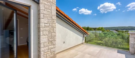 A balcony with a stone wall and a glass door leading to a room.
