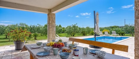 Un espace extérieur aménagé pour prendre les repas, avec vue sur une piscine et sur la verdure.