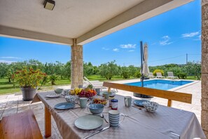 Ein Essbereich im Freien mit Blick auf einen Swimmingpool und viel Grün.