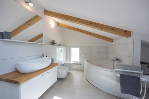Un baño moderno con una bañera independiente, un espejo grande y una viga de techo de madera.