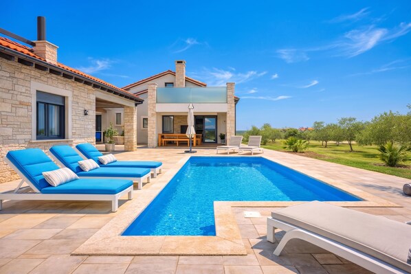 Ein modernes Haus mit Swimmingpool, Sitzgelegenheiten im Freien und Blick auf die Landschaft.