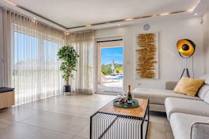 A modern living room with a sofa, a coffee table with a bottle and glasses, a potted plant, and a view of an outdoor area. - Sea View Villa Maria With Pool (Medulin)