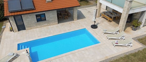 Una piscina con sillas de descanso, un patio cubierto y un edificio de piedra con tejado de baldosas.