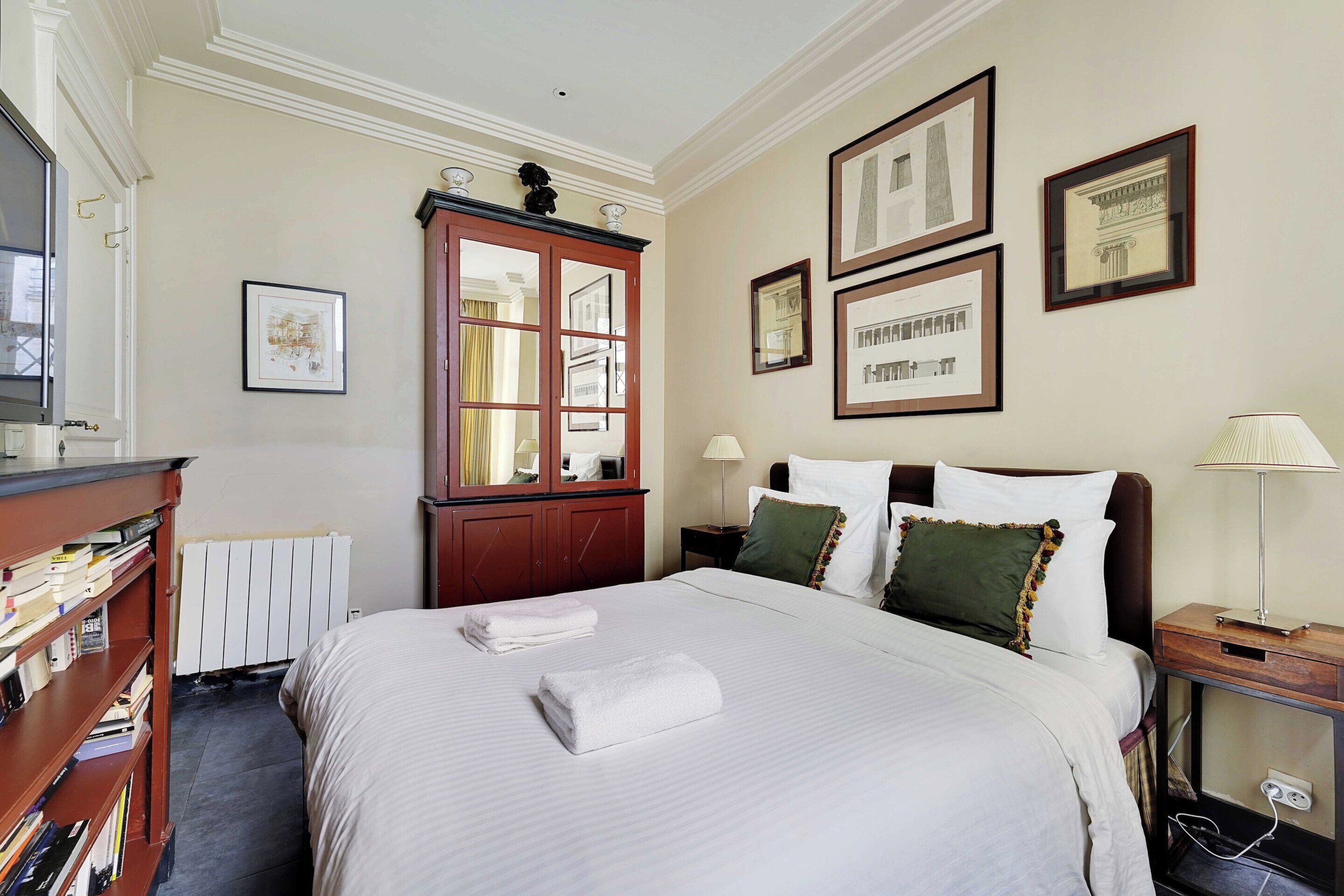 A neatly made bed with towels, a wooden cabinet, and framed pictures on the wall.