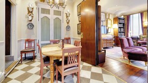 A dining area with a checkered floor, a wooden dining table, and matching chairs. There is a chandelier above the table and a bookshelf in the background. - Historic Elegance in the Heart of Marais - 6p/2br (Paris)