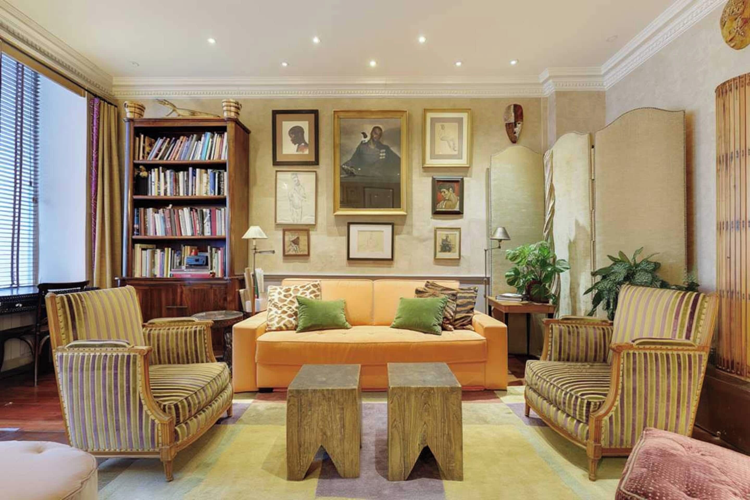 Een woonkamer met een bank, twee fauteuils, een boekenkast en lijstwerken aan de muur.