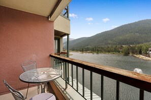A balcony with a table and chairs, overlooking a river and forested hills. - Lakefront Mountain Condo - Near Ski Base, Shops, Dining (Keystone)