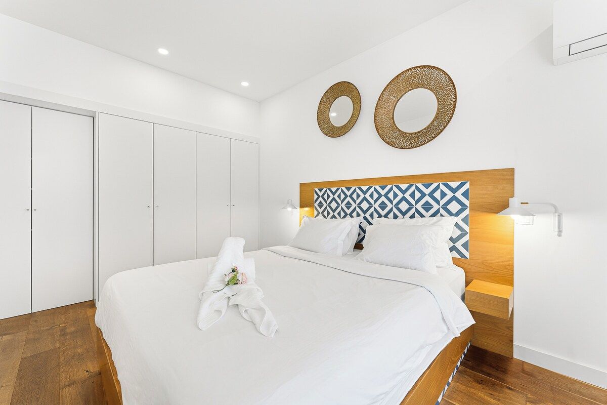 A hotel room with a large bed, a wooden headboard, and a wall-mounted mirror.