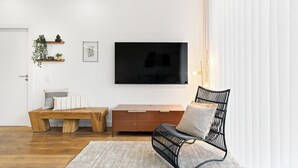 Uma sala de estar moderna com um banco de madeira, uma cadeira preta, um armário de madeira e uma TV de tela plana fixada na parede.