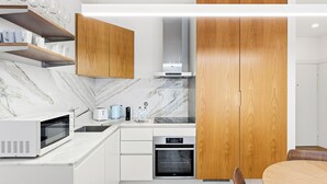 Uma cozinha moderna com armários brancos, forno embutido, micro-ondas e cafeteira.