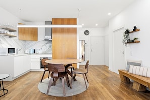 A modern kitchen with white cabinets, a wooden dining table, and a built-in oven. - Historic Porto Flat | Central Porto (Porto)