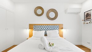 Quarto de hotel moderno com uma cama grande, dois espelhos redondos fixados na parede, uma cabeceira estampada e uma pequena mesa de cabeceira com um vaso de flores.
