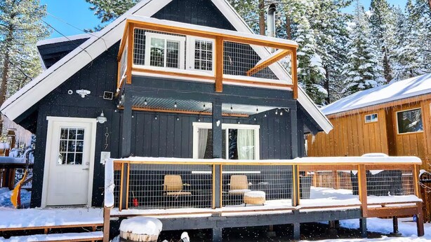 Eine zweistöckige Holzhütte mit Balkon, umgeben von schneebedeckten Bäumen.