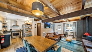 Eine geräumige Küche mit Holzbalken, ein Essbereich mit Holztisch und -stühlen sowie eine gemütliche Sitzecke mit einer Couch und Kissen.