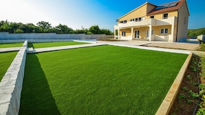A modern two-story house with a flat roof and a balcony, surrounded by a well-maintained lawn and a stone wall. - Villa Julija (Vodice)