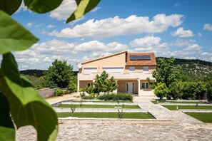A modern two-story house with a tiled roof, a garage, and a well-maintained garden with pathways and small trees. - Villa Julija (Vodice)