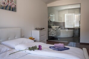 A hotel room with a bed, a nightstand, a bathroom with a bathtub, and a glass door leading to the bathroom. - Villa Julija (Vodice)