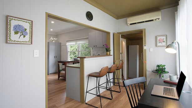 Una cocina moderna con armarios de madera, una isla central con taburetes altos y un ordenador portátil sobre una mesa.