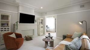 Una sala de estar moderna con un sofá de cuero marrón, un sillón rojo, una chimenea blanca y un televisor de pantalla plana montado en la pared.