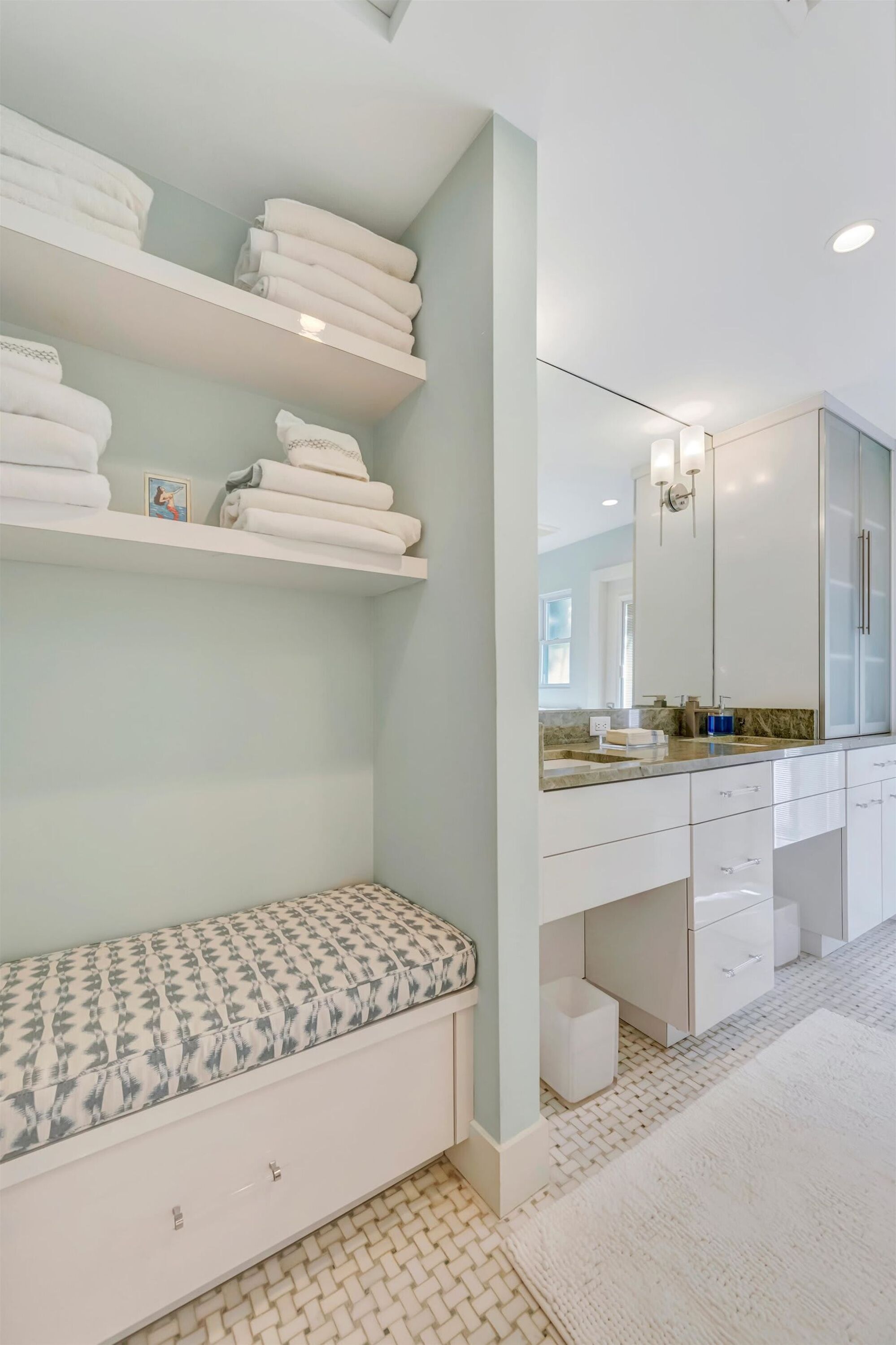 A modern bathroom with white cabinetry, a large mirror, and a bench with a patterned cushion.