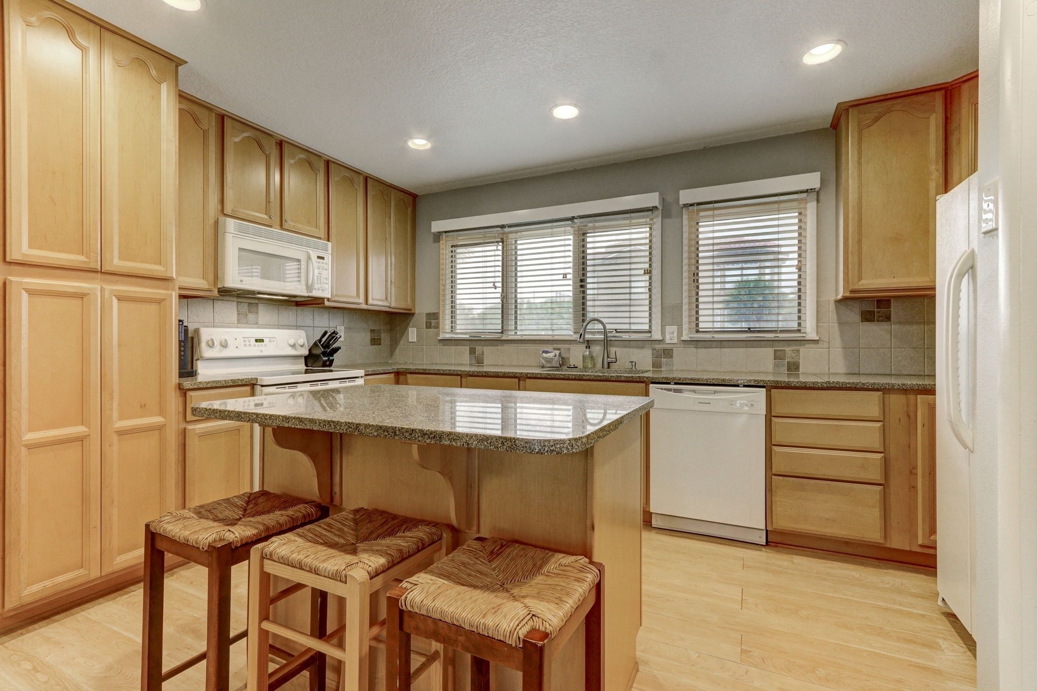 A kitchen with wooden cabinets, a microwave, a dishwasher, and a window with blinds.