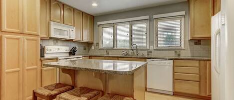 A kitchen with wooden cabinets, a microwave, a dishwasher, and a window with blinds.