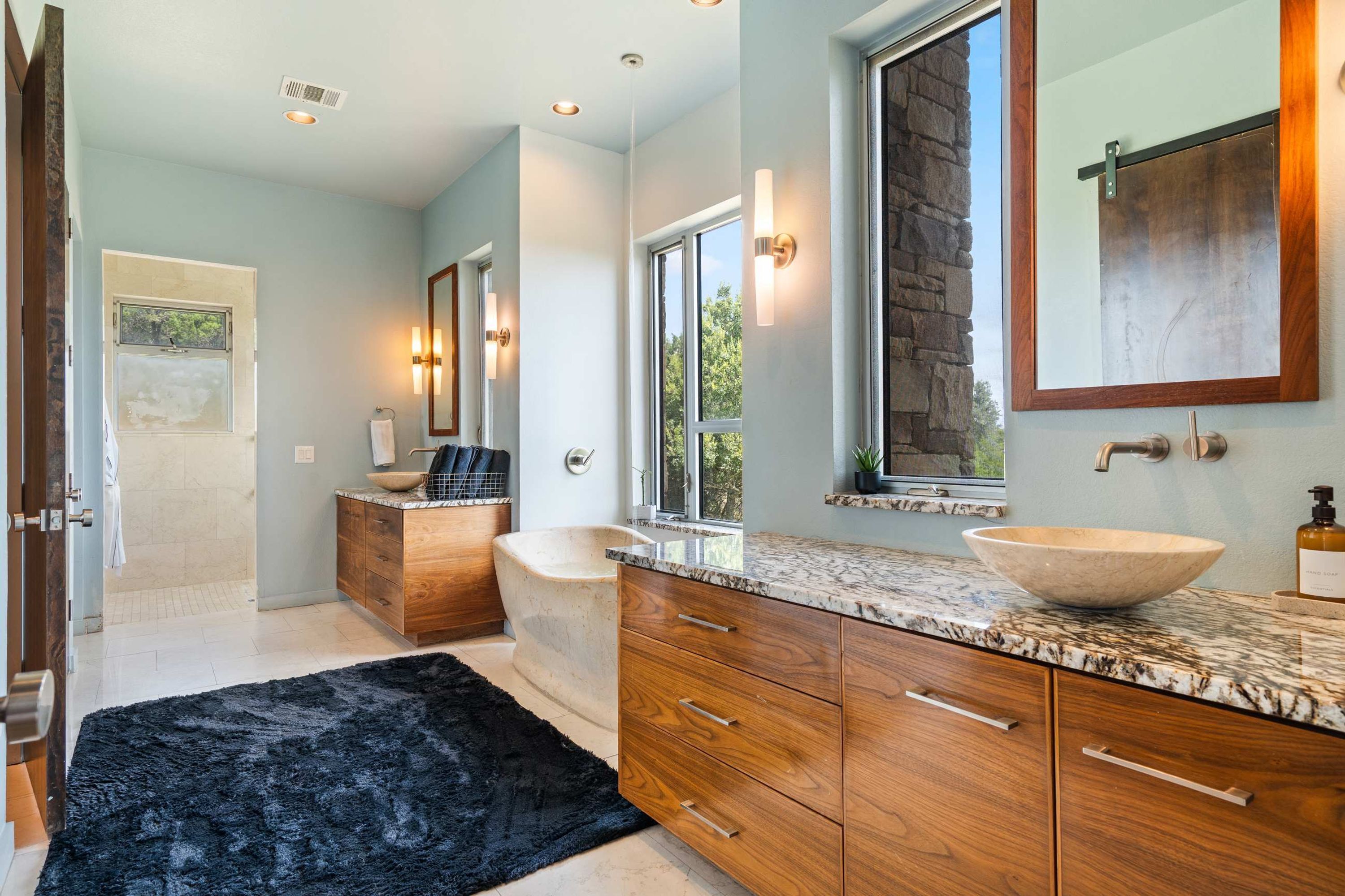 A modern bathroom with a large bathtub, wooden vanity, and a large mirror.