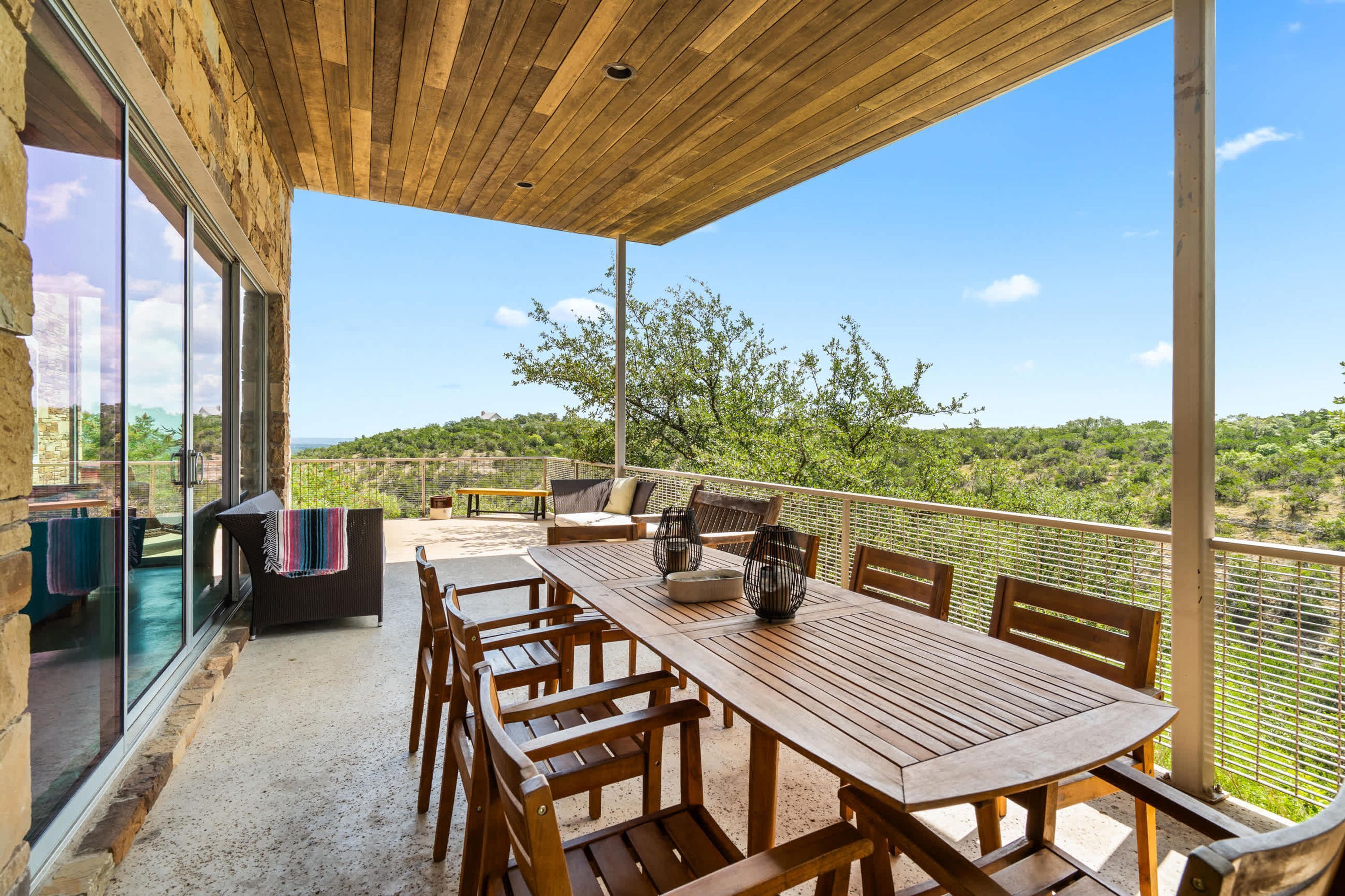 Un patio al aire libre con una mesa y sillas de madera, un sofá y vistas del paisaje.