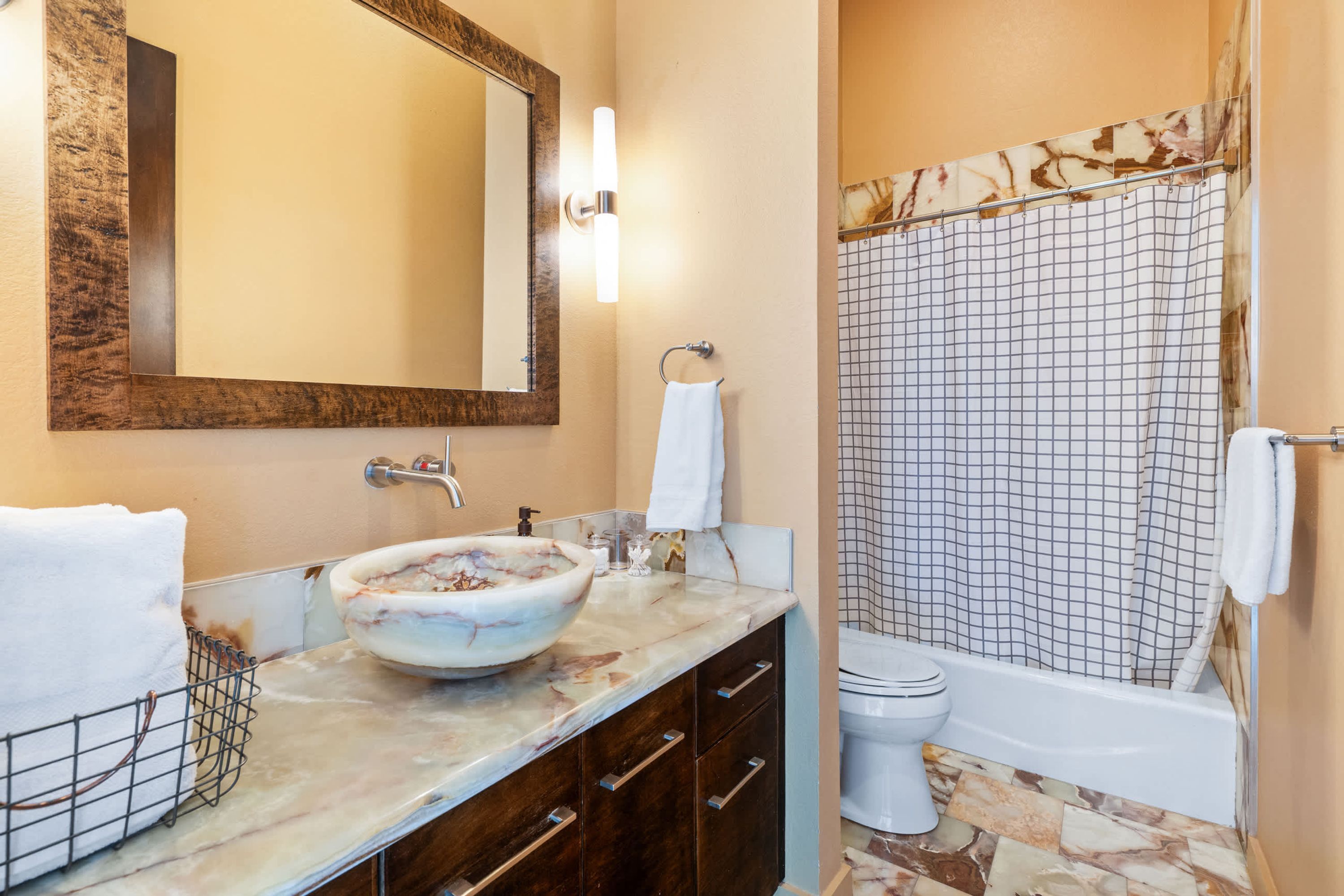 Une salle de bain avec un lavabo en marbre, un grand miroir, des toilettes et une douche avec un rideau à carreaux.