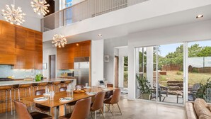 Una cocina moderna con una isla central, un comedor con una mesa grande y sillas, y vista al patio exterior.