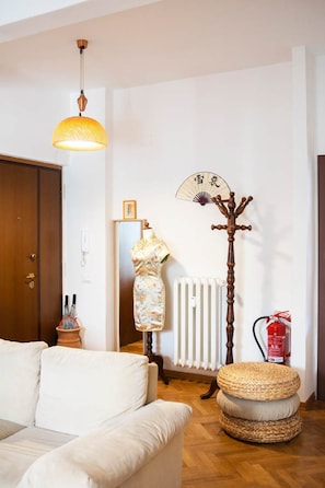 A living room with a sofa, a hanging lamp, a radiator, a wooden coat stand, and a fire extinguisher. - Casa Romitino Modern and Spacious Apartment (Florence)