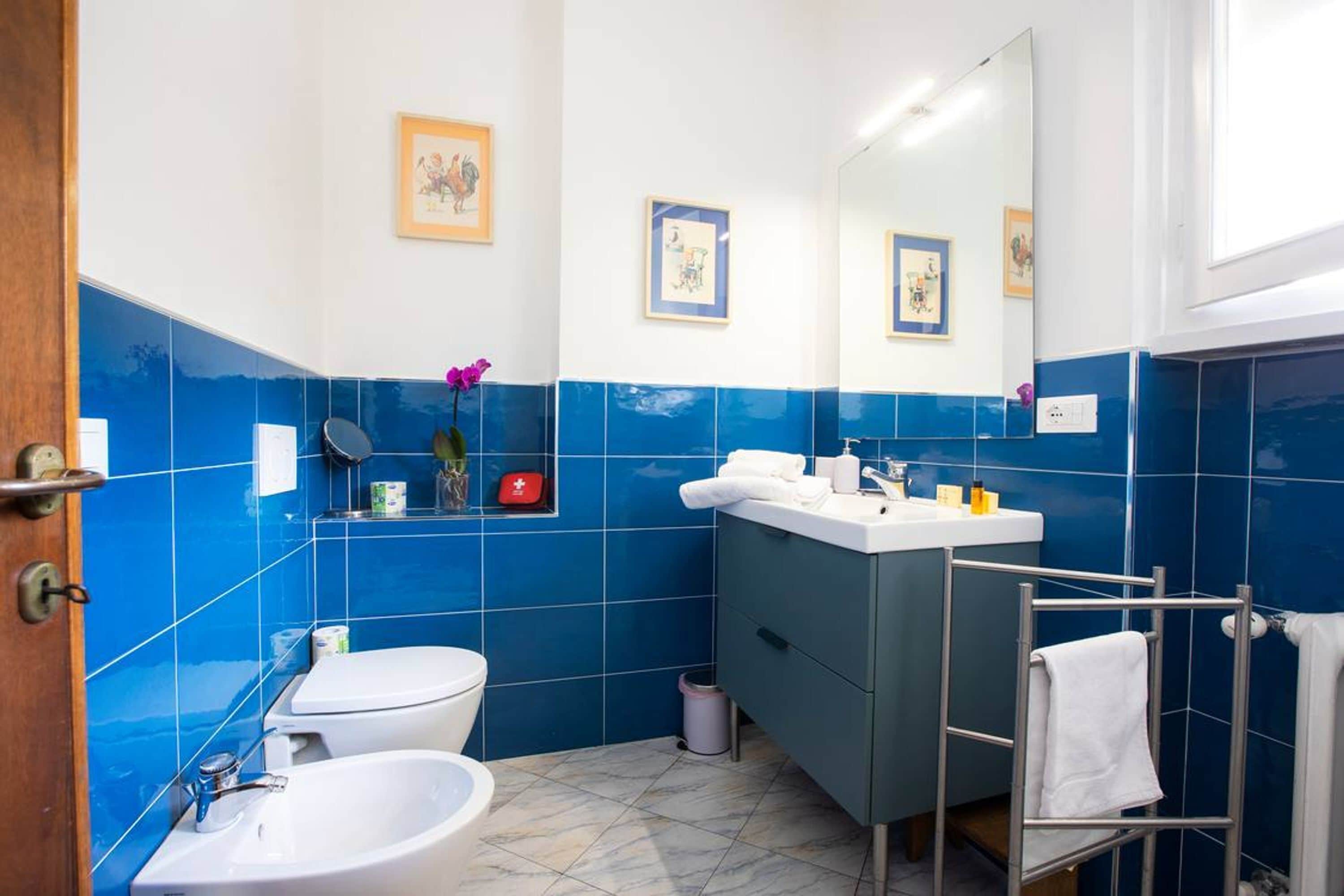 A bathroom with a white toilet, a white sink, and a bidet. There is a mirror above the sink, and a towel rack is visible.