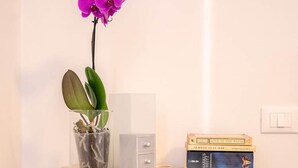 A small white desk with a glass vase containing a purple orchid and a potted plant, a stack of books, and a white drawer. - Casa Romitino Modern and Spacious Apartment (Florence)